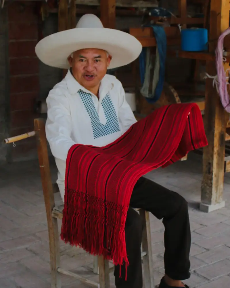 Artesano mostrando un textil rojo recién tejido sobre las piernas